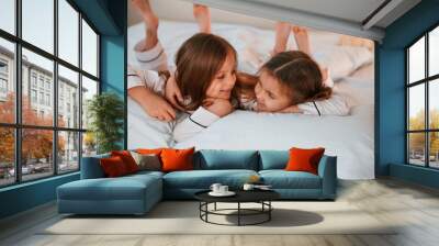 Smiling, laying down on the bed. Two little girls are playing and having fun together in domestic room Wall mural