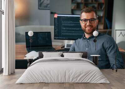 Software developer is sitting and posing. Man in formal clothes is working in the modern office. Using computer Wall mural