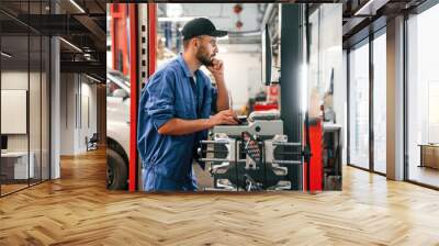 Standing by computer terminal. Auto mechanic working in garage. Repair service Wall mural