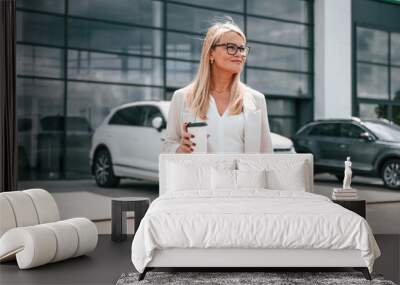 Standing outdoors near new automobile. Woman in white formal clothes is in the car dealership Wall mural