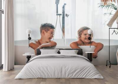 Two kids having fun and washing themselves in the bath at home. Posing for a camera Wall mural