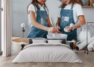 Two little girls in blue chef uniform mixing flour with eggs in plate on the kitchen Wall mural