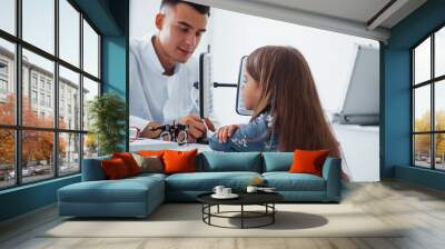 Two panels on the table. Young ophthalmologist is with little female visitor in the clinic Wall mural