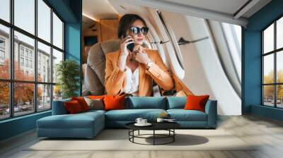 Uses phone. Young passenger woman in yellow clothes is flying in the plane Wall mural