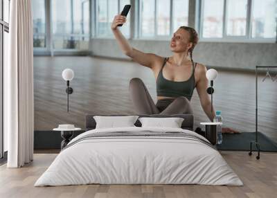 Using smartphone, break. Fitness woman in sportswear is indoors Wall mural