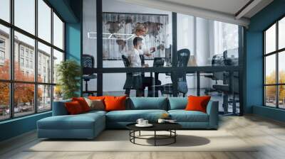 View through the glass. Two stockbrokers in formal clothes works in the office with financial market Wall mural