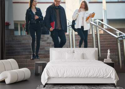 Walking down the stairs. Three young students are outside the university outdoors Wall mural