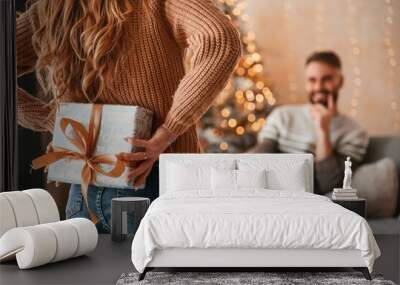 Woman is with gift box for the man. Lovely young couple are celebrating New Year at home Wall mural