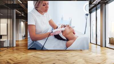 Woman lying down in spa salon and have face cleaning procedure by professional cosmetologist Wall mural