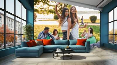 Women posing for the camera. Group of young people have a party in the park at summer daytime Wall mural