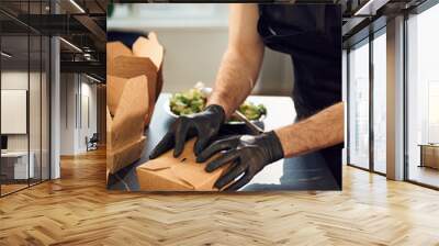 Working on the kitchen. Man is packing food into the paper eco boxes. Indoors, restaurant Wall mural