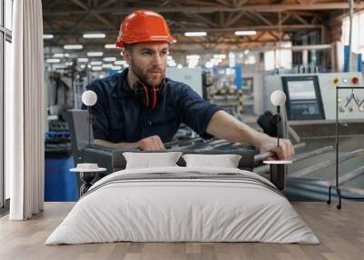 Working with machinery. Factory worker is indoors with hard hat Wall mural