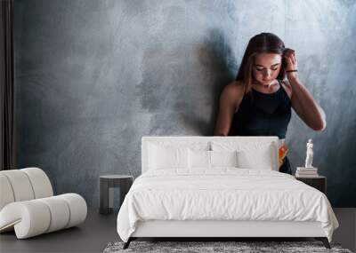 Young fitness woman with slim type of body and bottle of water is leaning on the wall Wall mural