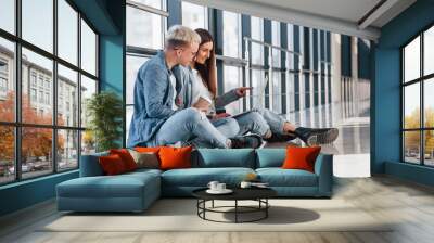 Young male and female students sitting together on the floor with laptop Wall mural