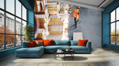 Young male worker in uniform is in the warehouse pushing pallet truck Wall mural