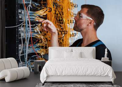 Young man in protective glasses works with internet equipment and wires in server room Wall mural