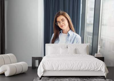 Young woman in glasses, formal clothes and with notepad standing indoors Wall mural