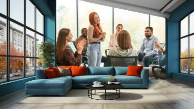 Young woman is standing and talking about herself. Group of people are having therapy meeting together Wall mural