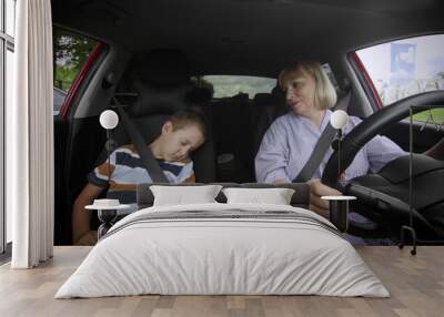 Grandmother and grandson are driving in the car. The boy fell asleep on the seat Wall mural