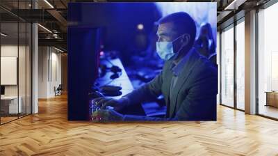 Side view of old man in costume and face mask chatting and surfing Internet in Modern computer club. Wall mural