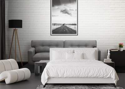 road picture in vertical art frame on wall. sofa, lamp, plant, glasses, book, coffee on table in liv Wall mural