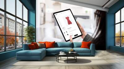 Woman buys a dress online with tablet concept. Modern e-commerce clothing website. Living room in background Wall mural