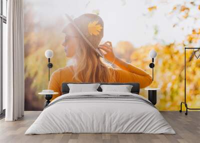 blonde in a yellow jacket on a background of autumn nature. the frame is lit by sunlight. A young woman in a gray hat looks at the autumn forest. Portrait of a woman in autumn Wall mural