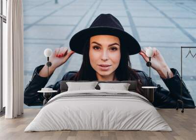 Close-up Fashion Woman portrait of a young girl posing in a city in Europe. Smiling pretty brunette woman in fashionable black hat and leather jacket outdoors. spring walk around the city Wall mural