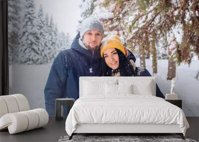 loving couple walks through the winter forest and plays with snow in cold weather. young couple is walking in a winter park. guy and girl in dark blue jackets. Winter forest. Active winter holidays. Wall mural