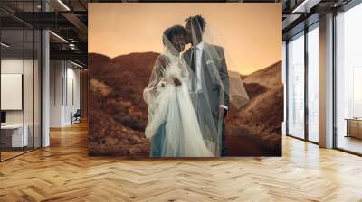 Newlyweds stand under bridal veil, smile and kiss in canyon at sunset. Wall mural