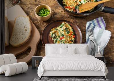 A piece of frittata with spinach and red pepper on a plate and a cutting board with bread, rustic style, top view Wall mural