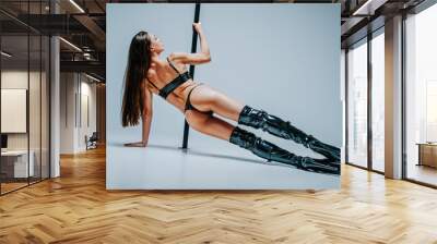 Young sexy woman pole dancing in leather clothing and boots on white background Wall mural