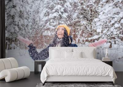 Portrait of a brunette woman in a yellow hat on a background of a winter forest. Smiling girl is playing with snow in the park. Wall mural