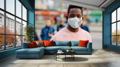 Portrait of young African man with a medical protective mask on his face at city street. Wall mural