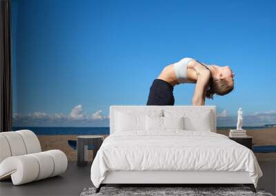 Young slim girl doing yoga on the beach on a sunny morning, stretching before doing sports Wall mural