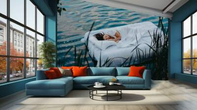 Woman sleeps on a mattress floating in the water among plants. Wall mural