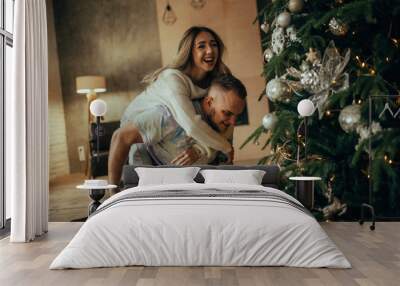 Young couple having fun and laughing on background of Christmas tree. Wall mural