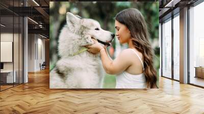 Young dwarf woman embraces Malamute dog in park. Wall mural