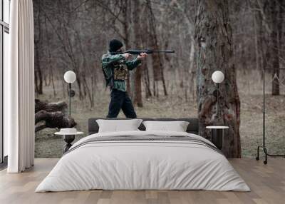 Young man aims from pump gun weared in body armor and balaclava. Wall mural