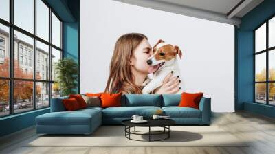 Cute young woman kisses and hugs her puppy jack russell terrier dog. Love between owner and dog. Isolated on white background. Studio portrait. Wall mural