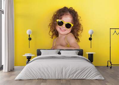 Little girl in a bathing suit and sunglasses on a yellow background Wall mural