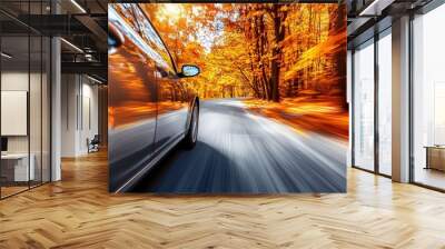 A black car speeding through an autumn forest road with colorful leaves as the sun sets in the background Wall mural