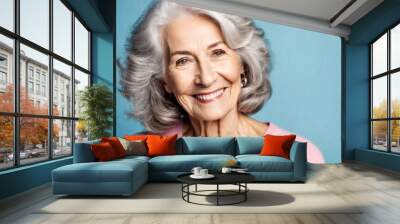 Happy beautiful elderly senior model with grey hair in a pink t-shirt on a blue background, portrait of beauty mature old woman with hairstyle and makeup, healthy face skin with wrinkles, dental care Wall mural