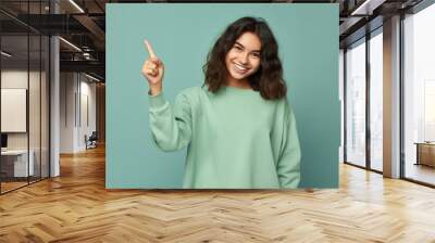 Excited young ginger teenager girl smiling and pointing index finger up at copy space expressing wow emotion standing isolated on green background studio copy space, advertisement concept. High Wall mural