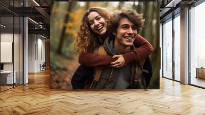 Happy young man carrying his beautiful smiling pretty woman on his back at the park, having fun together. Boyfriend giving piggyback ride on shoulder to his beautiful girlfriend in autumn. High Wall mural