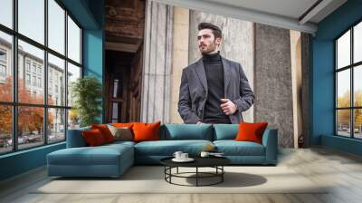 Handsome bearded young man outdoor in winter fashion, wearing black turtleneck sweater and woolen blazer jacket in city setting Wall mural