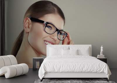 Pretty smiling female wearing stylish eyeglasses posing in studio. Concept of vision and ophthalmology.  Wall mural