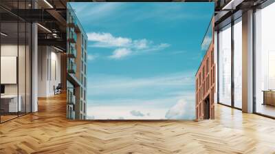 Two modern buildings facing each other. Separated by the blue sky with clouds. Abstract photo. Wall mural