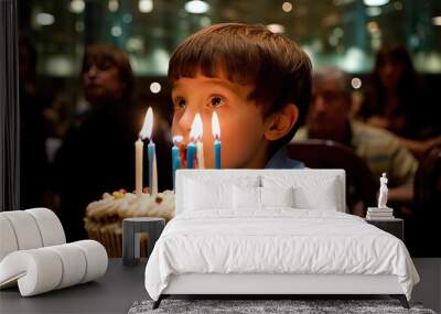 Little boy looks on birthday cake making wish. His eyes mirror the warmth of the birthday candles. Wall mural