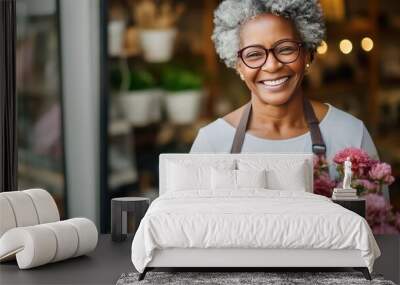 Portrait of happy African American woman standing in her flower shop. Cheerful middle aged saleswoman is waiting for customers of the flower shop. Standing at the entrance and smiley looking at camera Wall mural